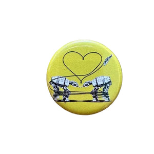 Round yellow badge button with black illustrations of two robots forming a heart 