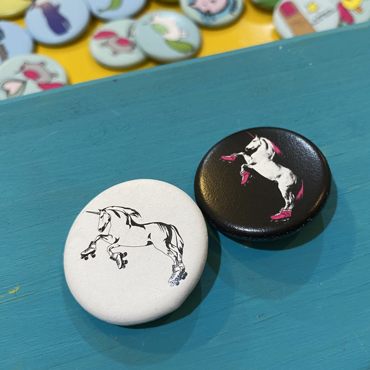 Two buttons with unicorn designs on a blue surface