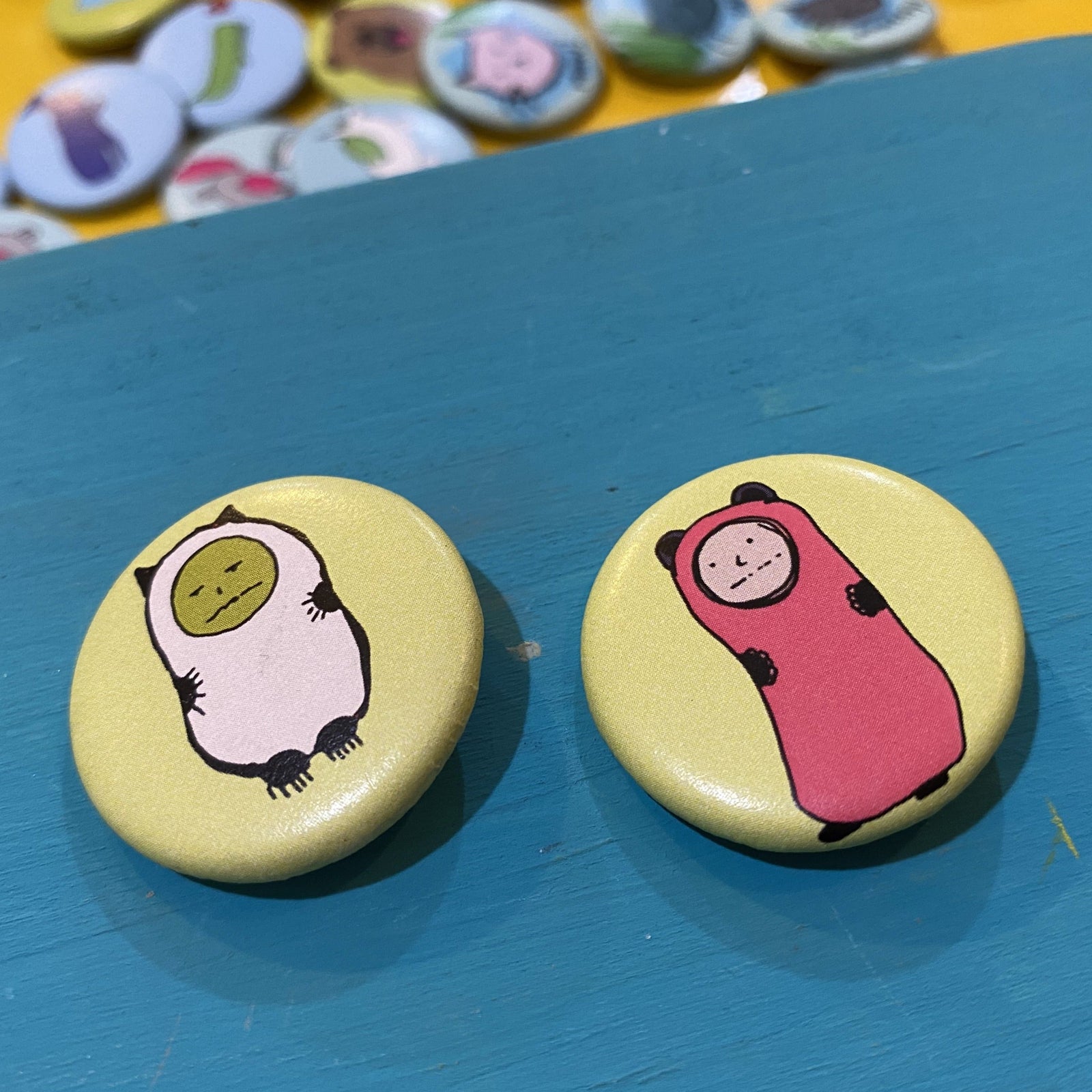 Two round buttons with cartoon characters on a blue surface, with more buttons in the background.