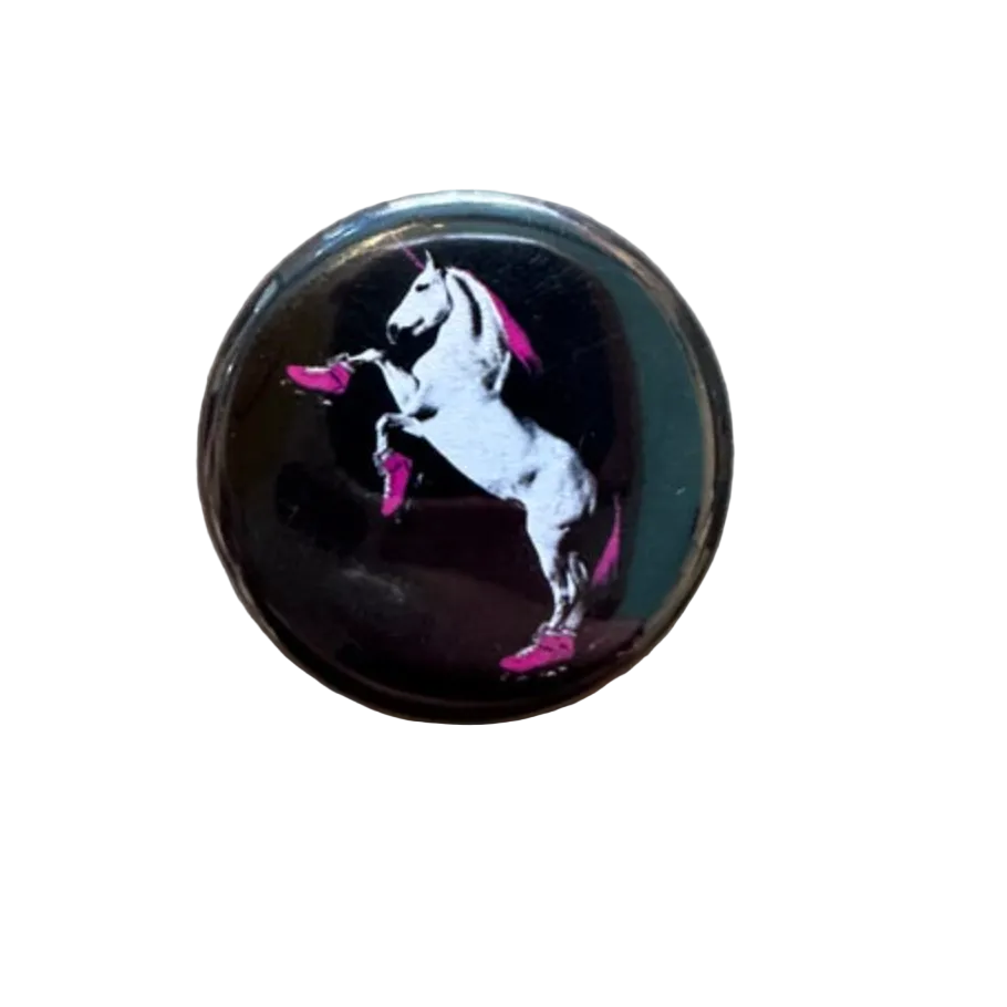 Round black button pin with a design of a unicorn wearing pink rollerskates. 
