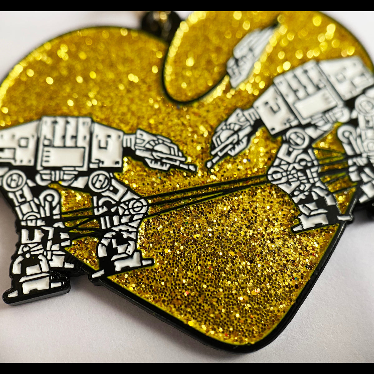 A closeup of a gold glitter keychain with two robots surrounded by a heart against a white background. 