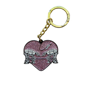 A pink glittery keychain with gold hardware featuring a design of two robots surrounded by a heart. 