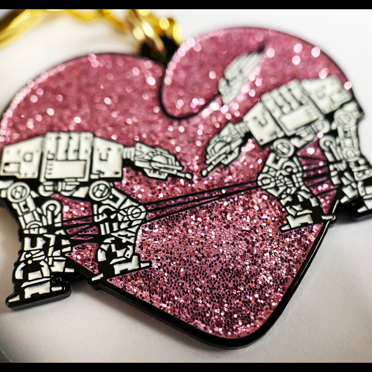 A closeup of a glittery pink keychain with two robots surrounded by a heart against a white background. 