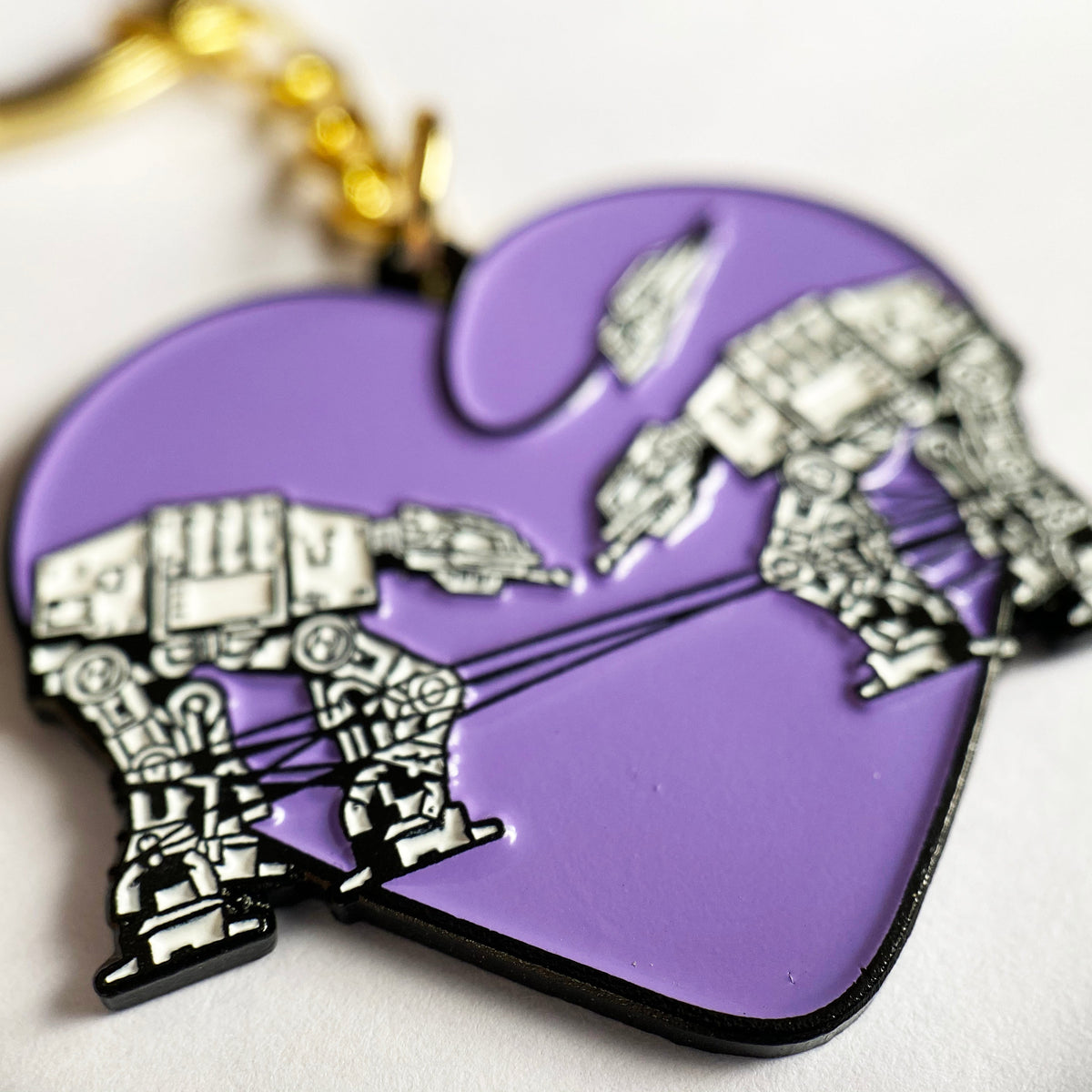 A closeup of a purple keychain with two robots surrounded by a heart against a white background. 