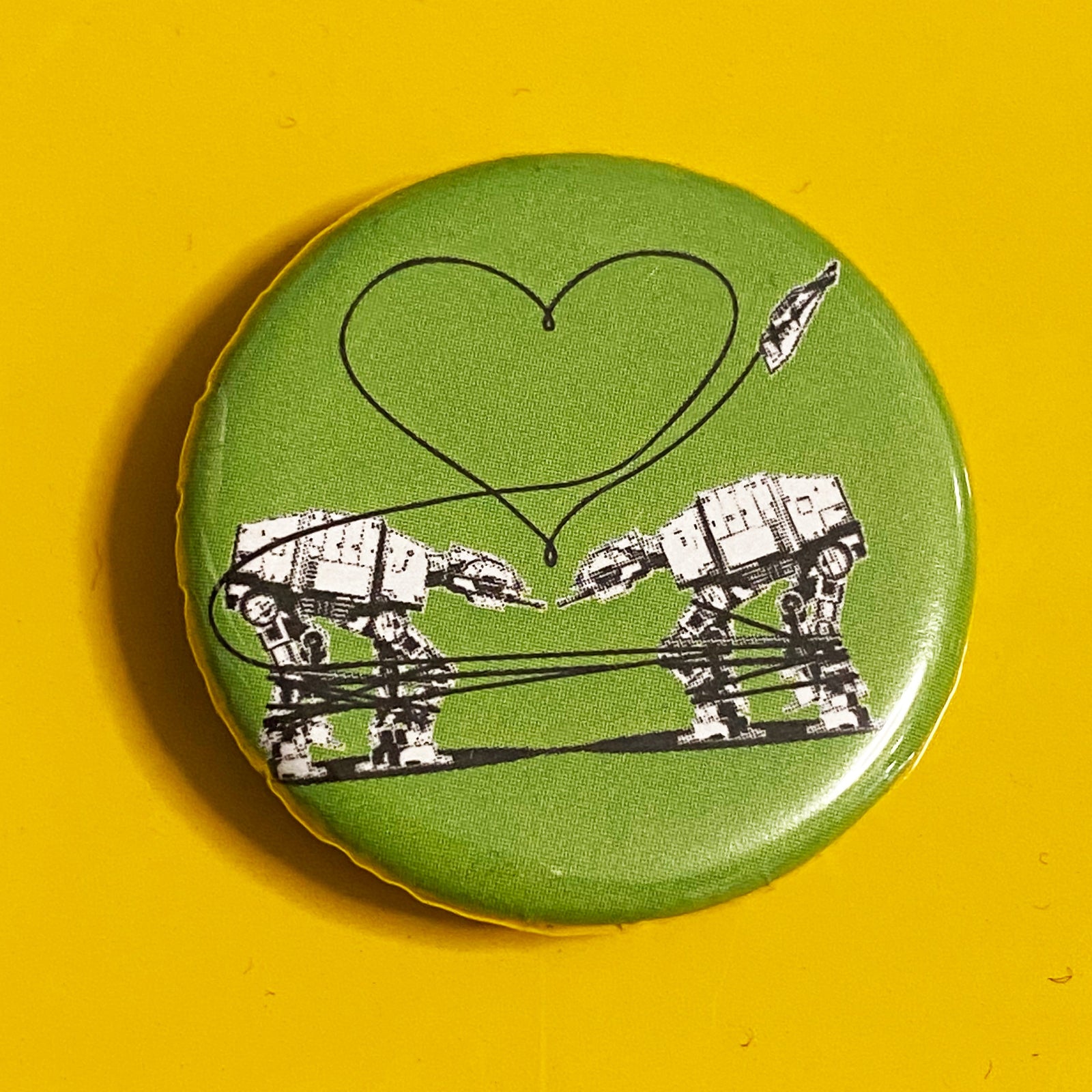 A round green magnet featuring a design of two AT-ATs from Star Wars with a heart above them. 