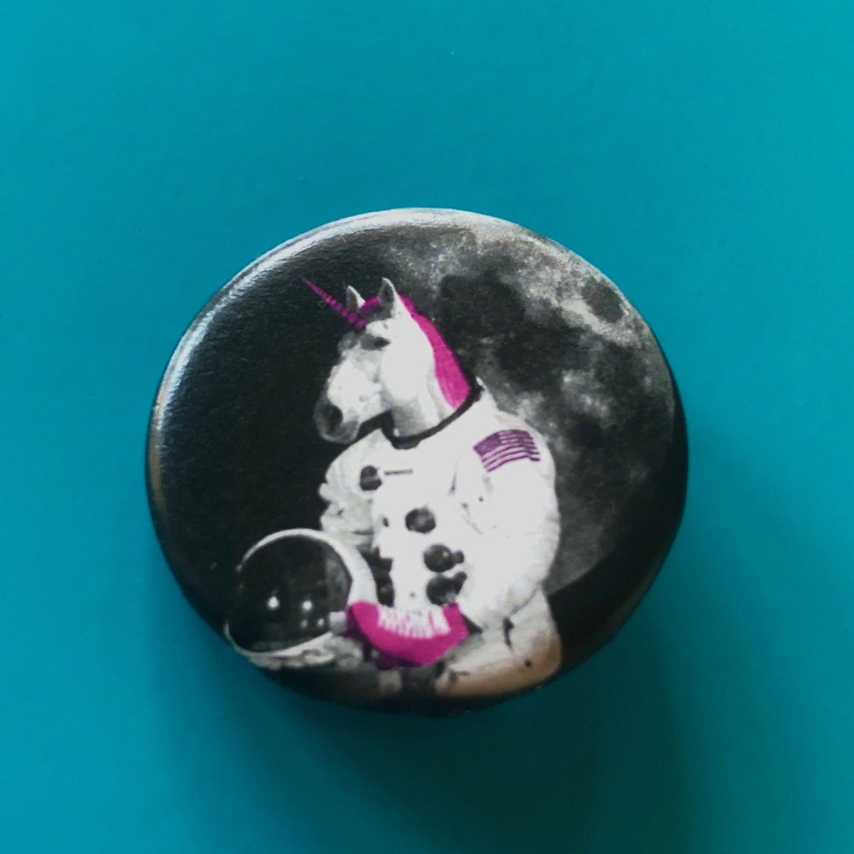 A round magnet featuring a design of a unicorn with a pink mane and horn wearing pink roller skates and dressed as an astronaut with a moon in the background. 