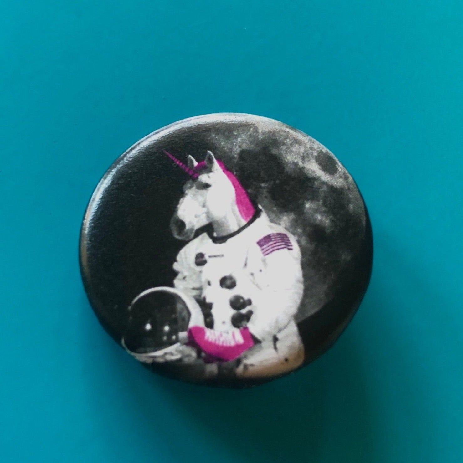 A round magnet featuring a design of a unicorn with a pink mane and horn wearing pink roller skates and dressed as an astronaut with a moon in the background. 