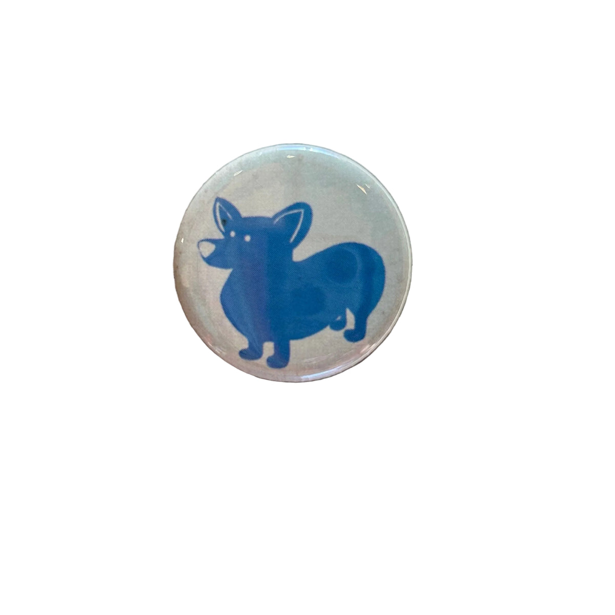 A round white magnet with a drawing of a blue corgi. 