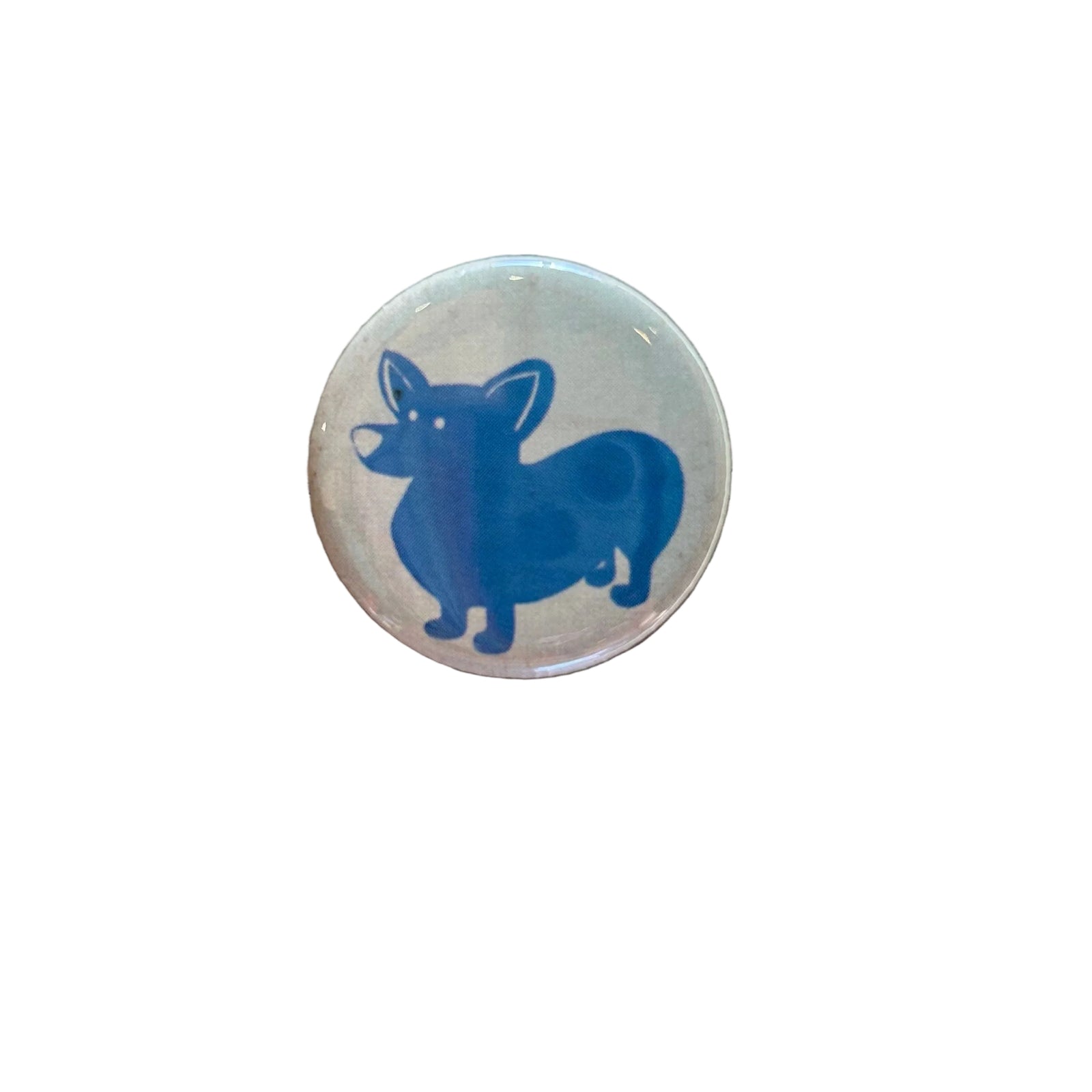 A round white magnet with a drawing of a blue corgi. 