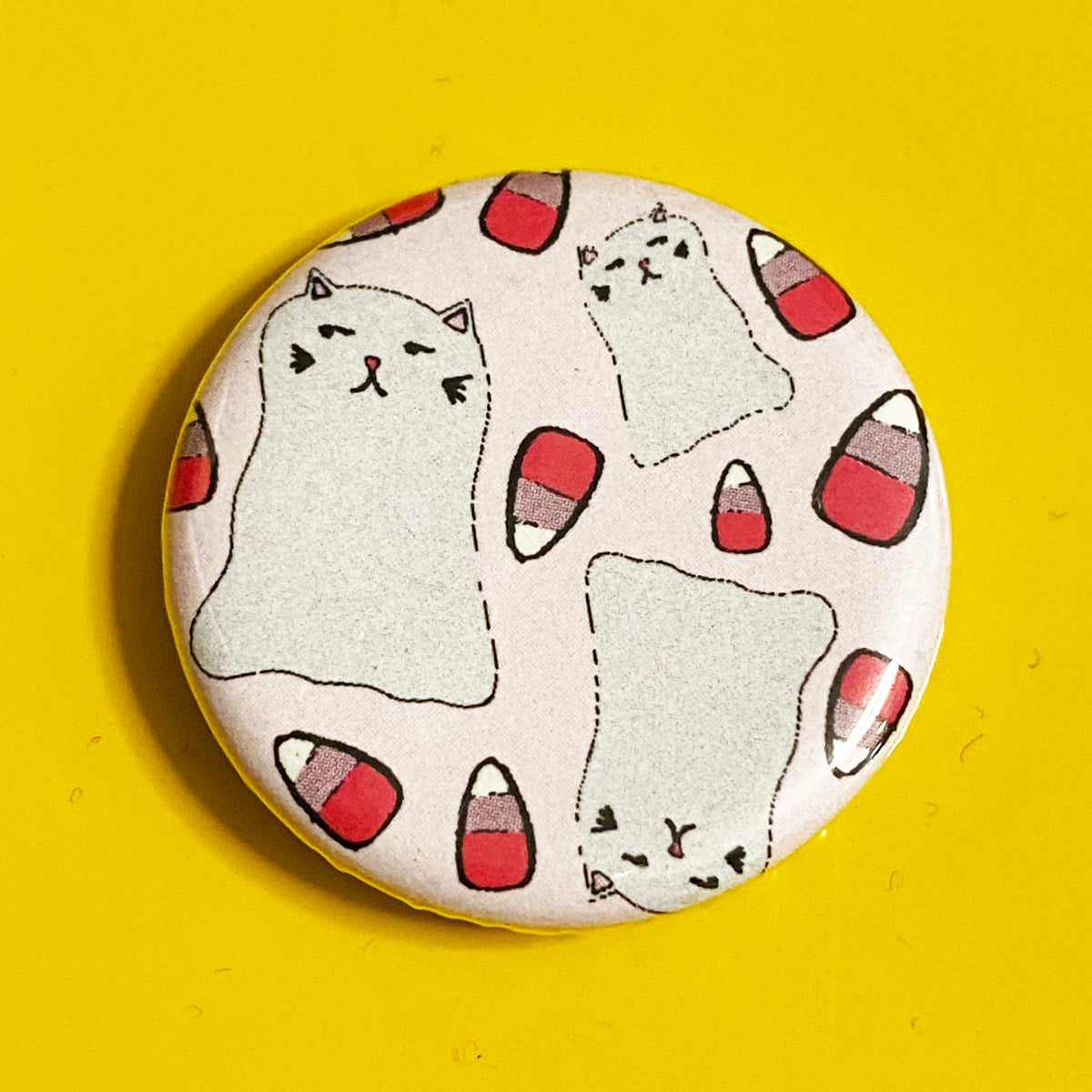 A round pink magnet with illustrations of pink candy corn and ghost cats