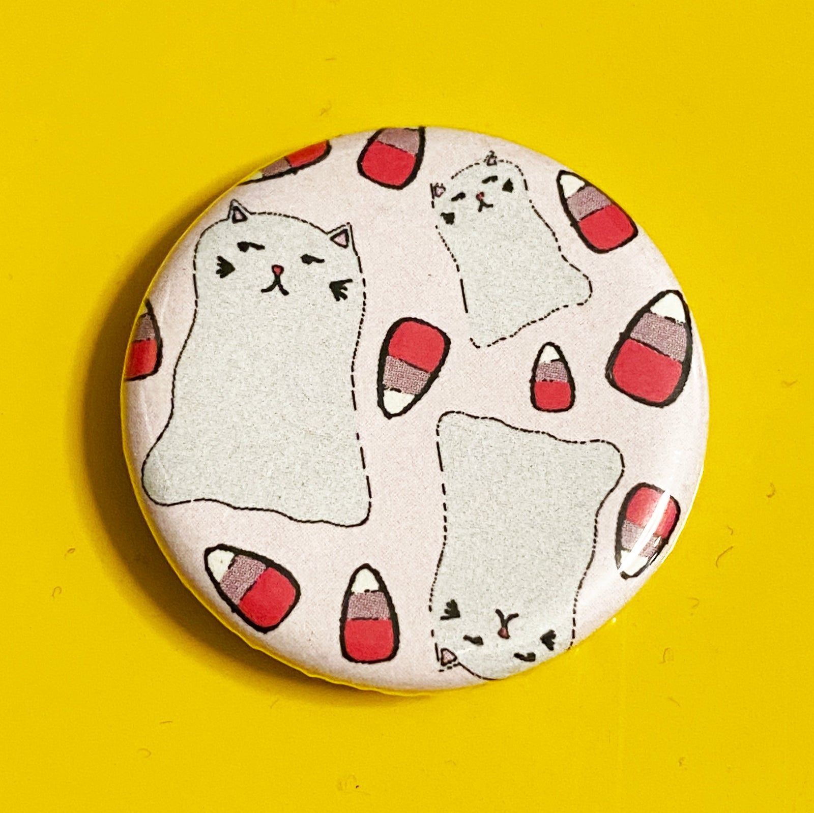 A round pink magnet with illustrations of pink candy corn and ghost cats