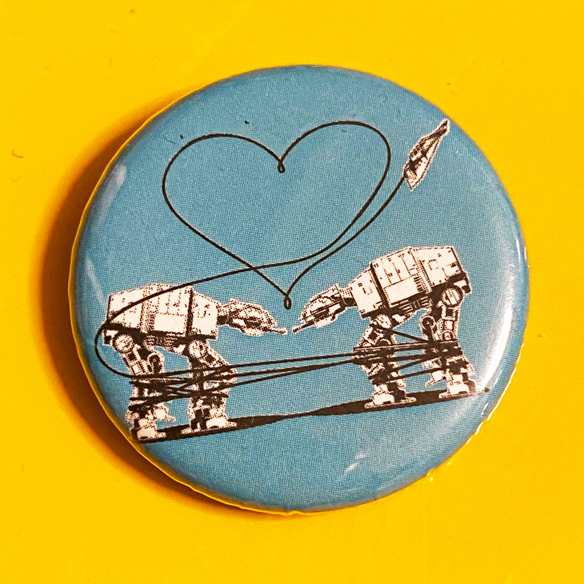 A round blue magnet featuring a design of two AT-ATs from Star Wars with a heart above them. 