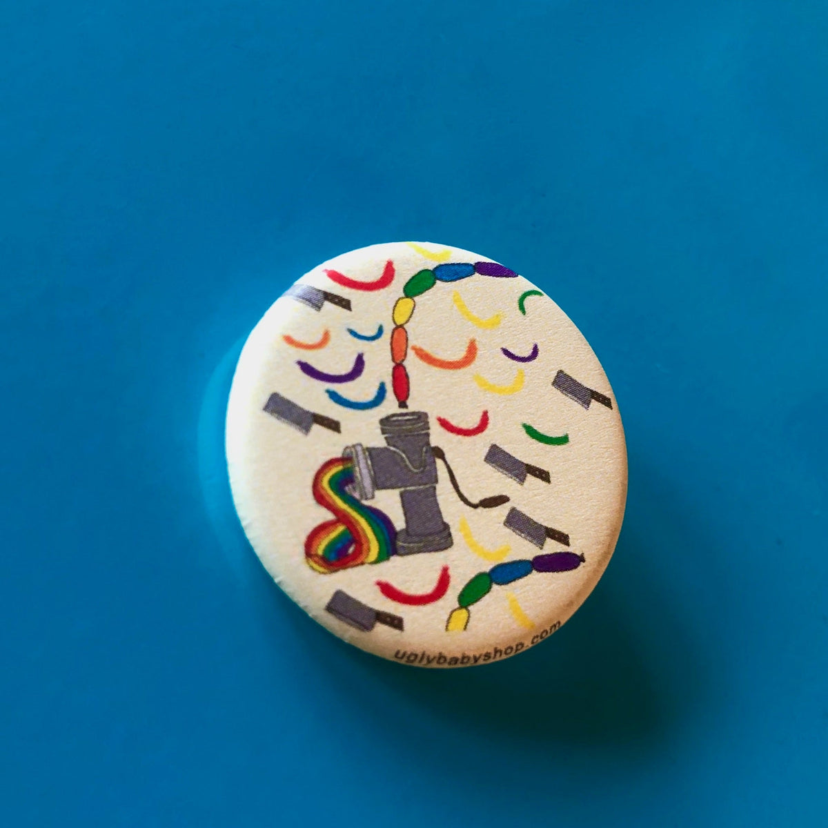 A round magnet with illustrations of a meat grinder, cleavers, and rainbow sausages, against a blue backdrop