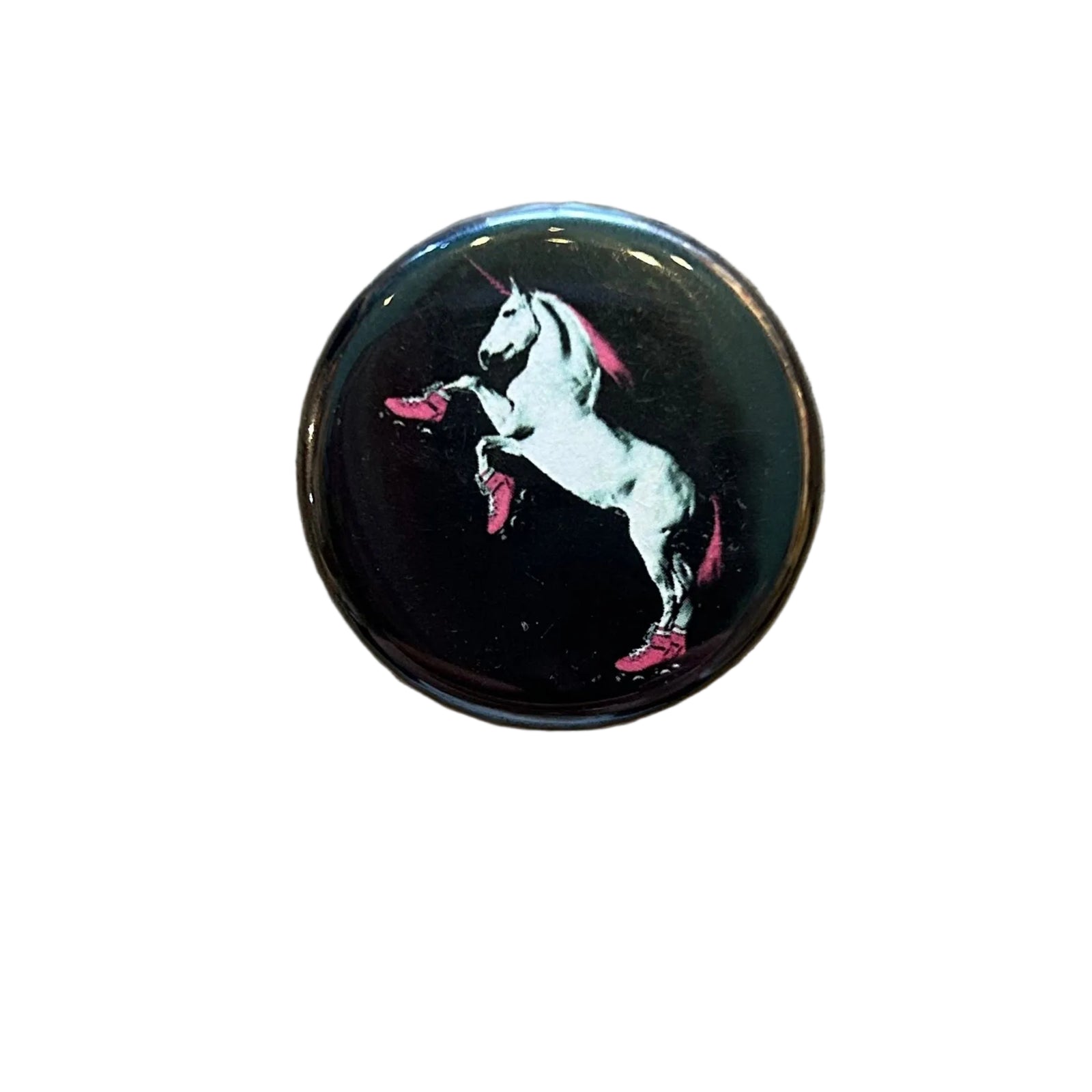 A round black magnet with an illustration of a white unicorn with a pink mane and tail wearing pink roller skates and rearing up. 