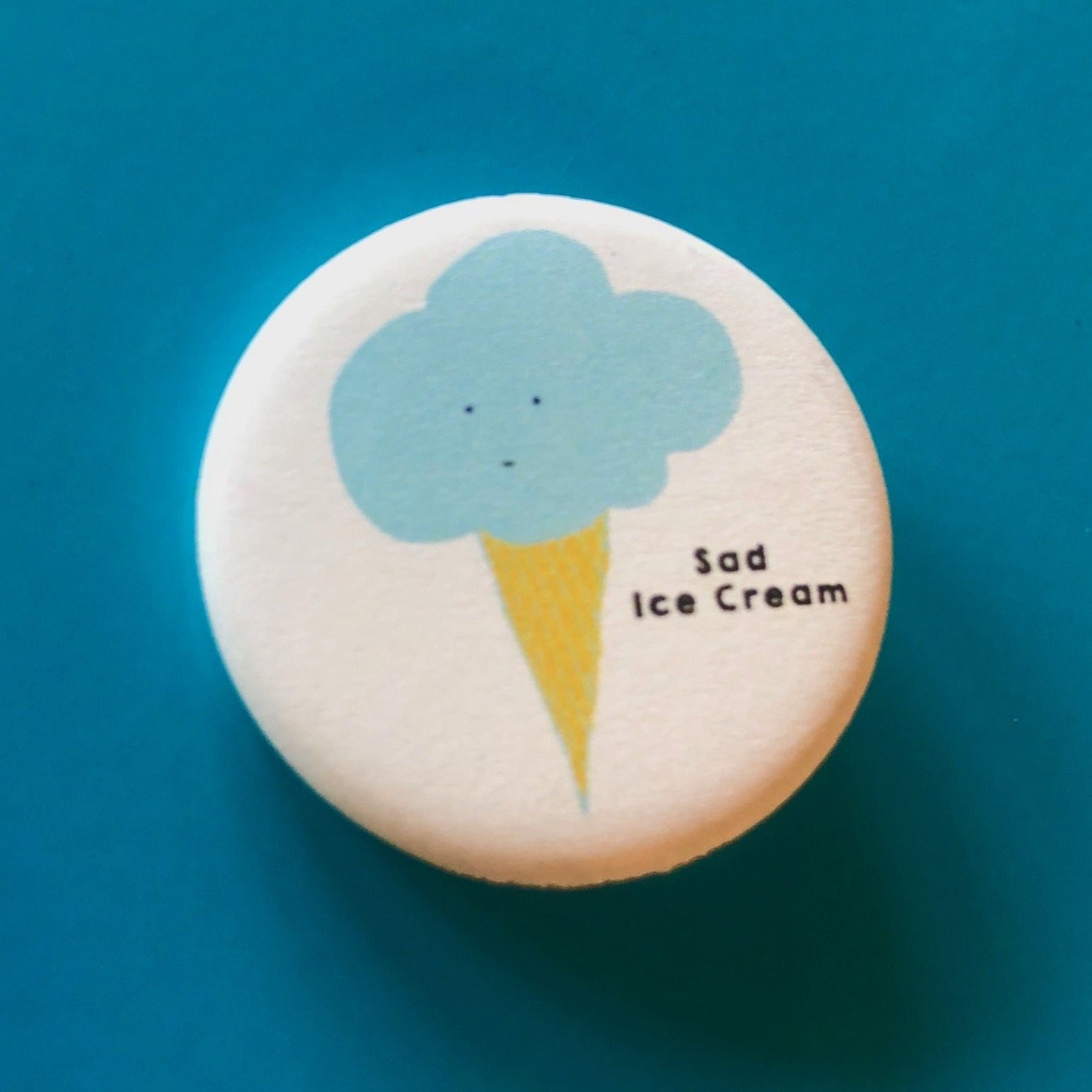 A round white magnet with an illustration of an ice cream cone and text that says "Sad Ice Cream" against a blue background. 