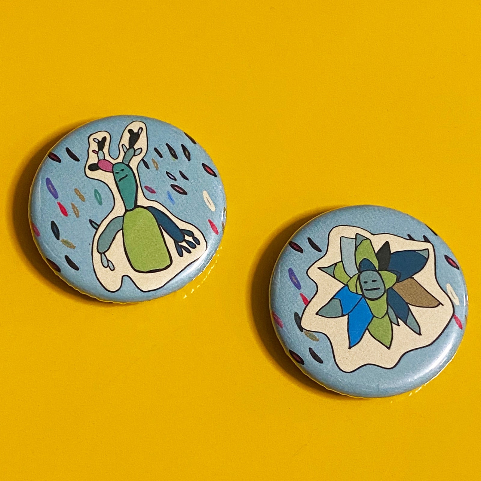 Two round illustrated magnets featuring succulent designs in blues and greens against a yellow backdrop.