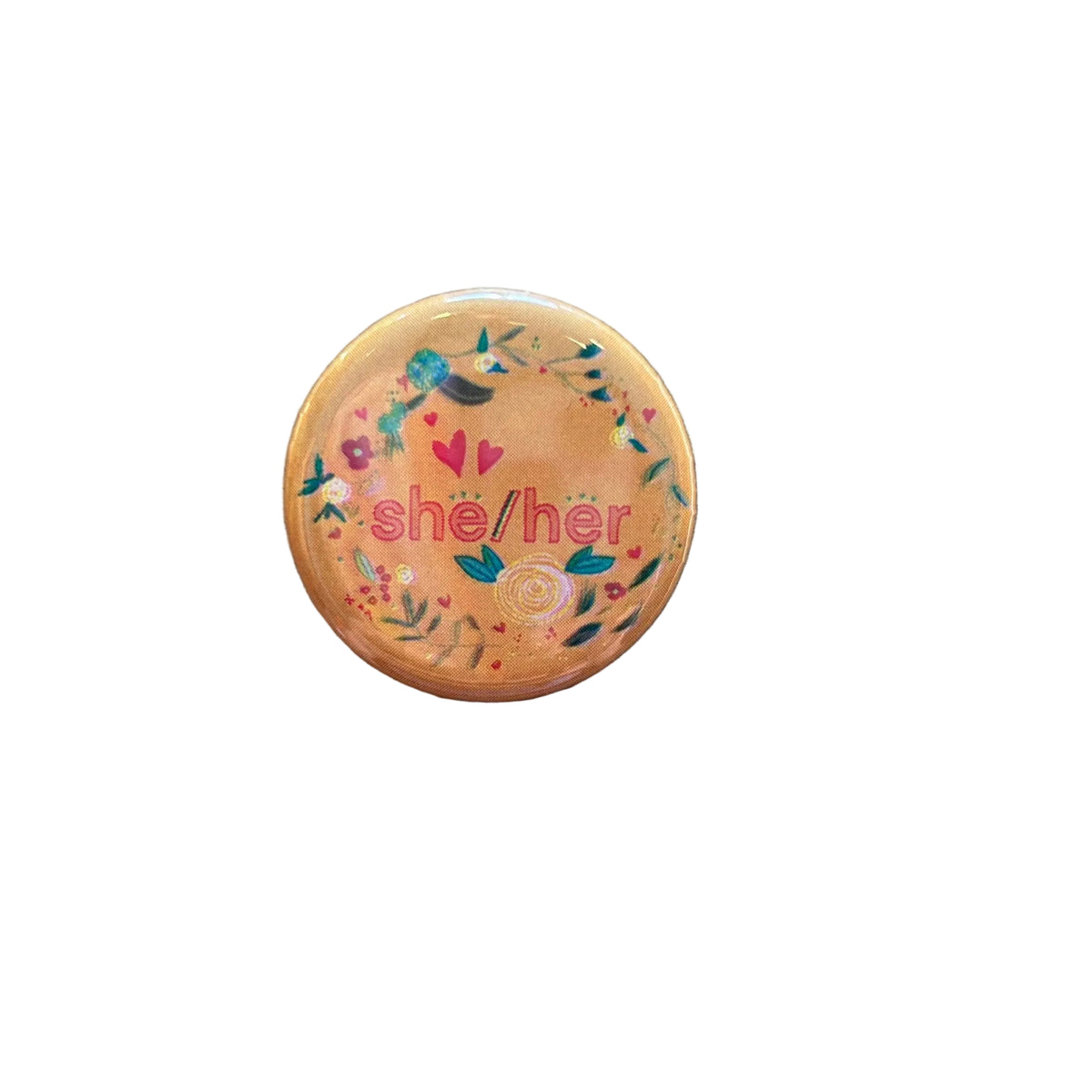 A round orange button with various floral doodles and text that says "she/her"