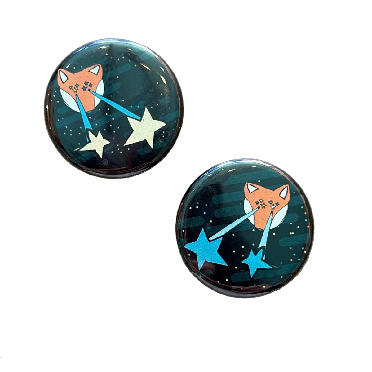 Two round black magnets with illustrations of foxes shooting lasers out of their eyes against a white background. 