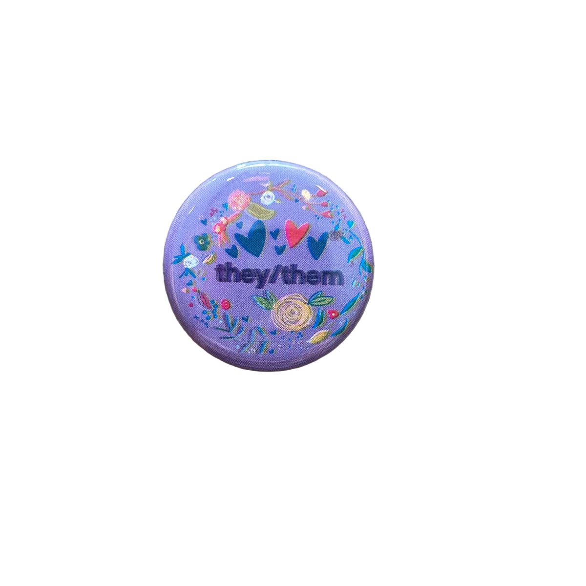 A round purple magnet featuring various floral doodles and text that says "they/them"