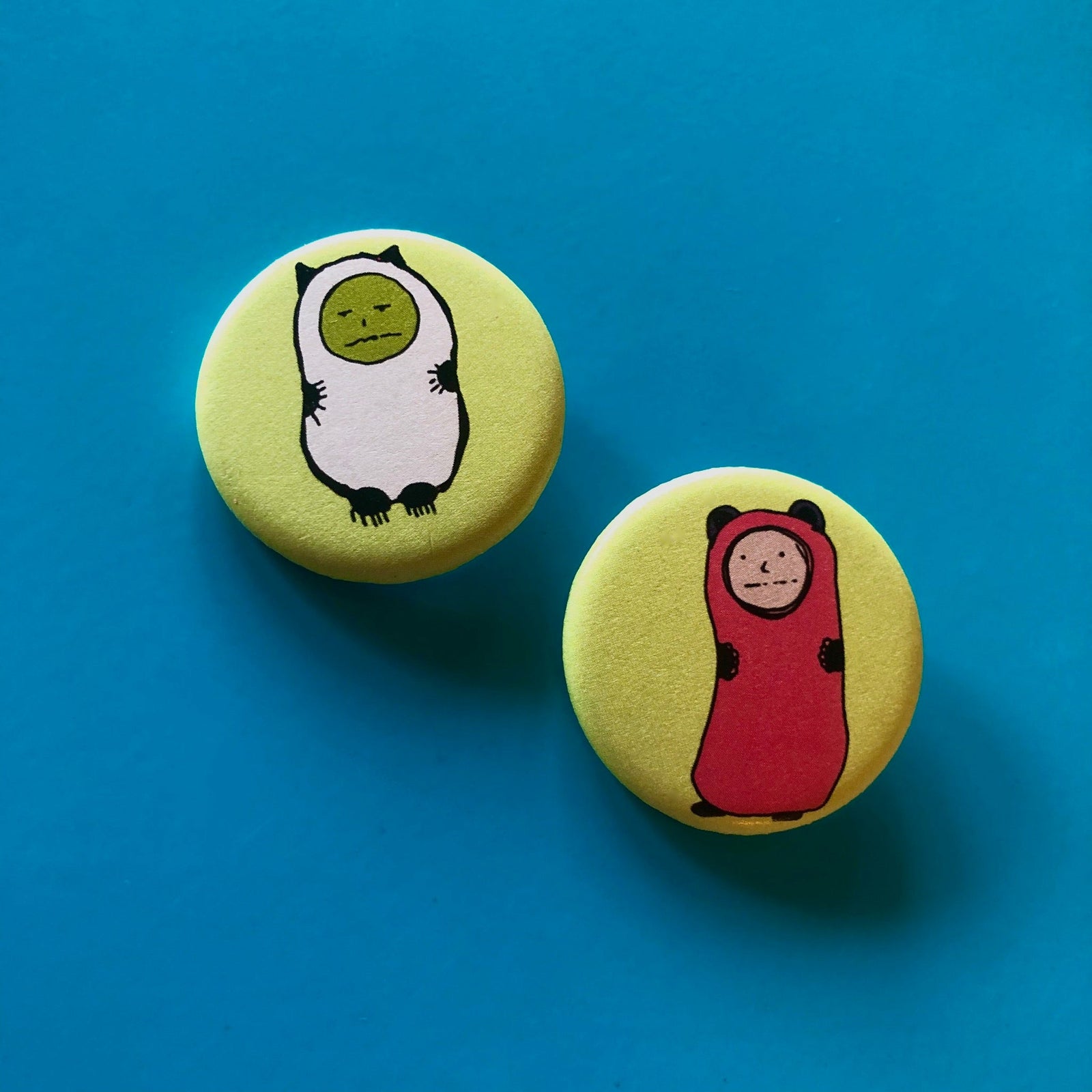 Two light green magnets with cartoon character illustrations on them against a blue background. 