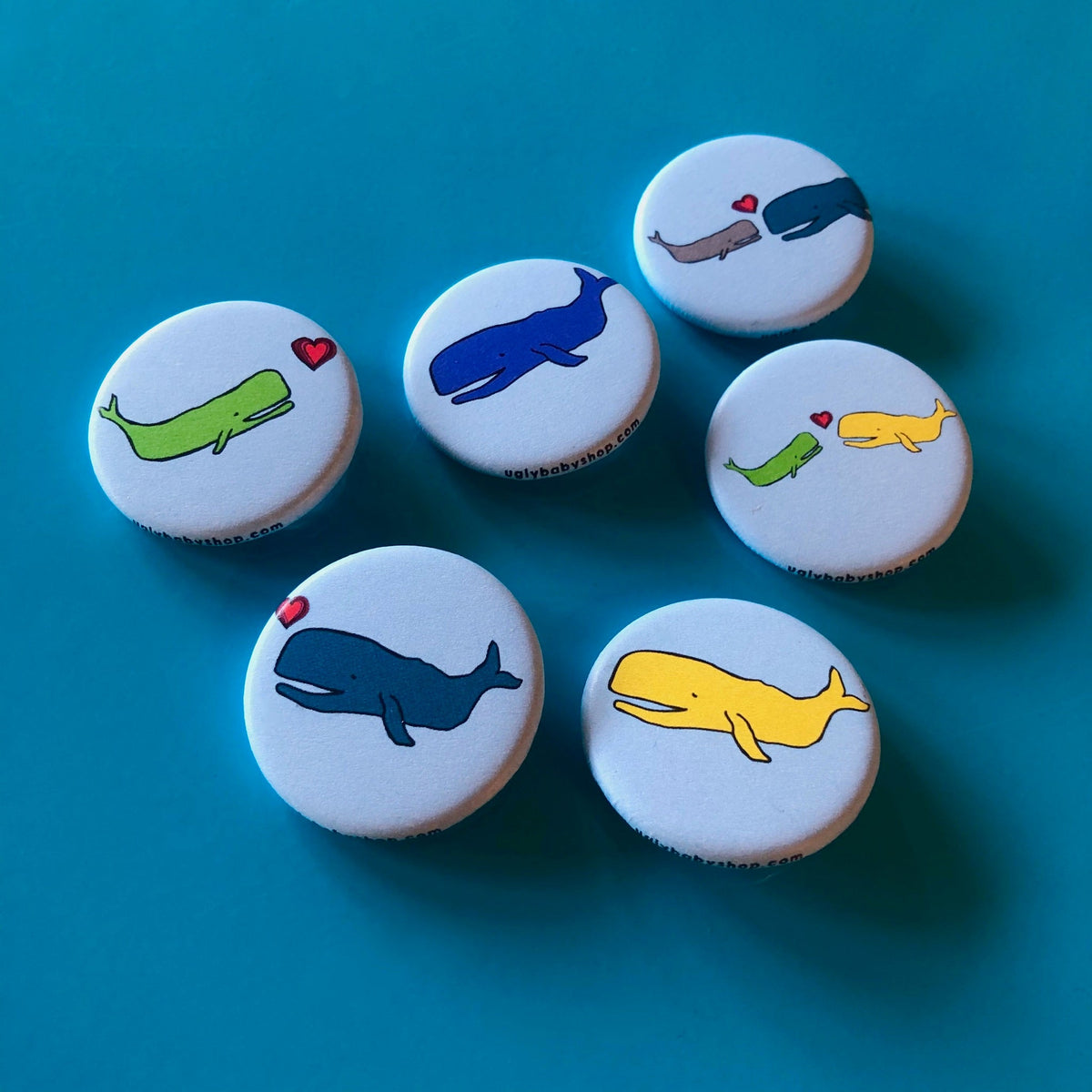 A grouping of light blue magnets with dark blue, green, gray, and yellow whale illustrations on them against a blue background. 