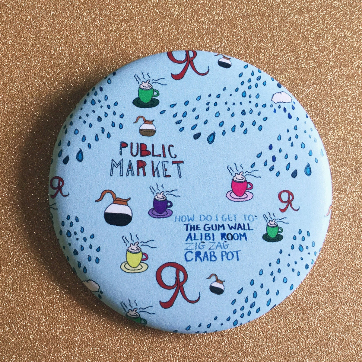 A round blue magnet with various Seattle-themed illustrations on a glittery gold backdrop. 