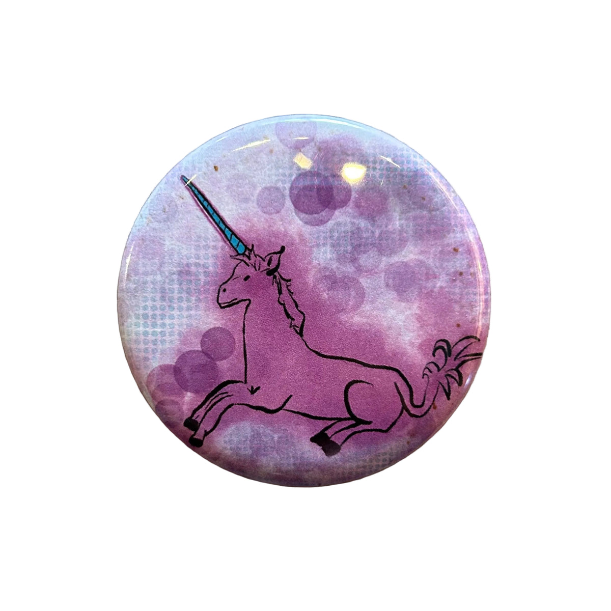 A round magnet featuring a pink and purple watercolor unicorn design with a black outline.