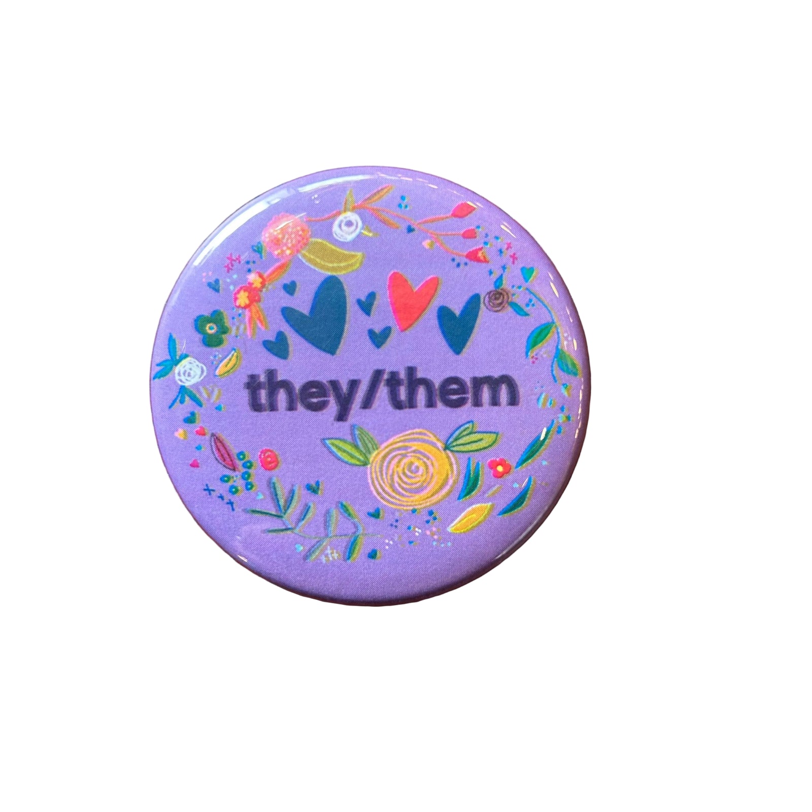Round purple magnet with a floral border and text in the middle that says "they/them"