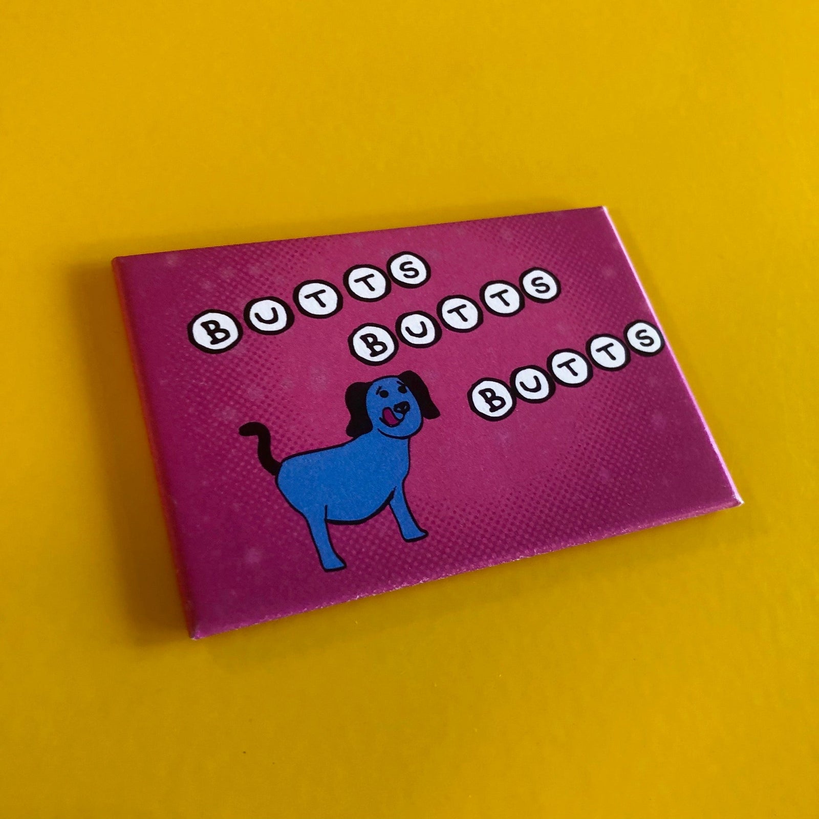 Purple rectangular magnet with a drawing of a blue dog and text that says "BUTTS BUTTS BUTTS"