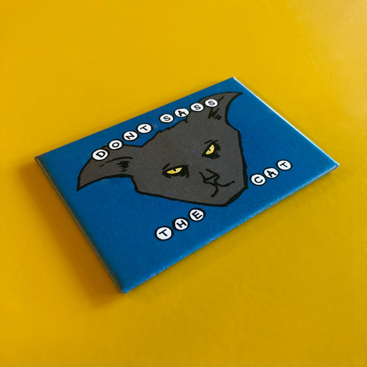 Blue rectangular magnet with an illustration of a cat's face and text that says "DON'T SASS THE CAT"