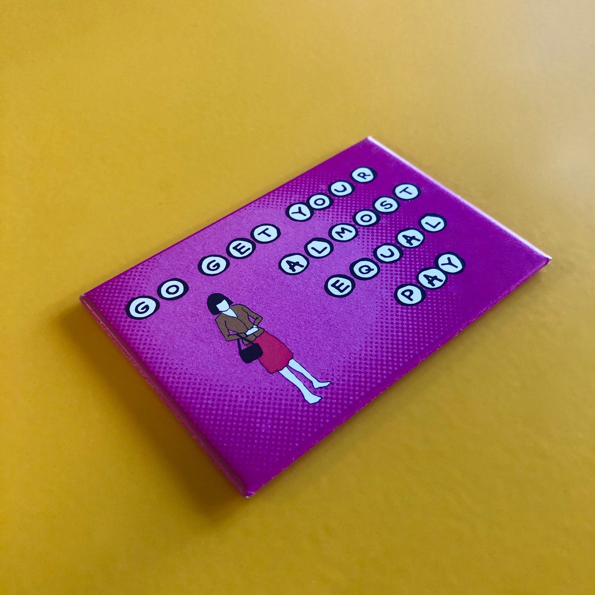 Purple rectangular magnet with an illustration of a woman holding a purse and text that reads "GO GET YOUR ALMOST EQUAL PAY" against a yellow background. 