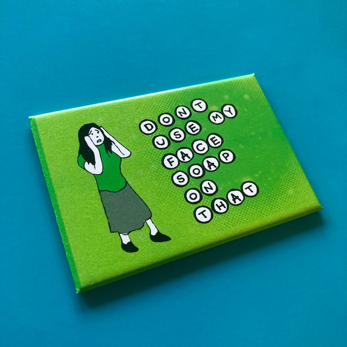 Green rectangular magnet with an illustration of a distressed woman and text that says "DON'T USE MY FACE SOAP ON THAT"
