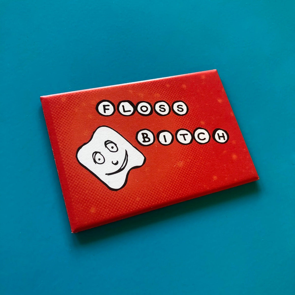 Red rectangular magnet with a illustration of a smiling tooth and text that reads "FLOSS BITCH" against a blue background. 
