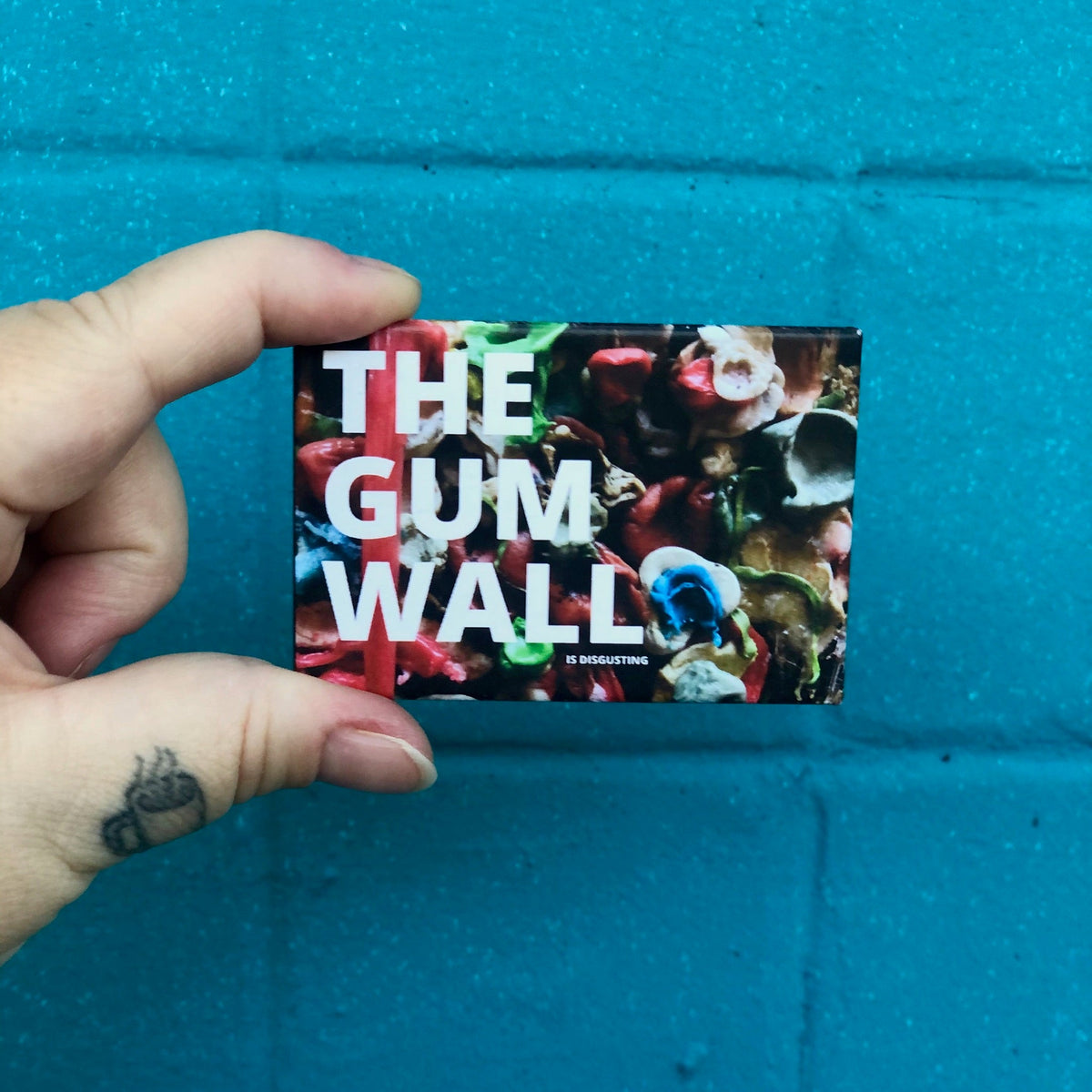 Rectangular magnet with text that says "THE GUM WALL IS DISGUSTING" with a picture of chewed gum in the background. 
