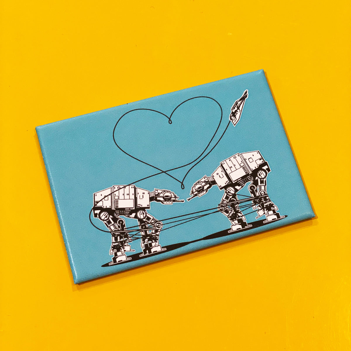 A blue rectangular magnet with an illustration of two AT-ATs from Star Wars with a heart above them, against a yellow backdrop