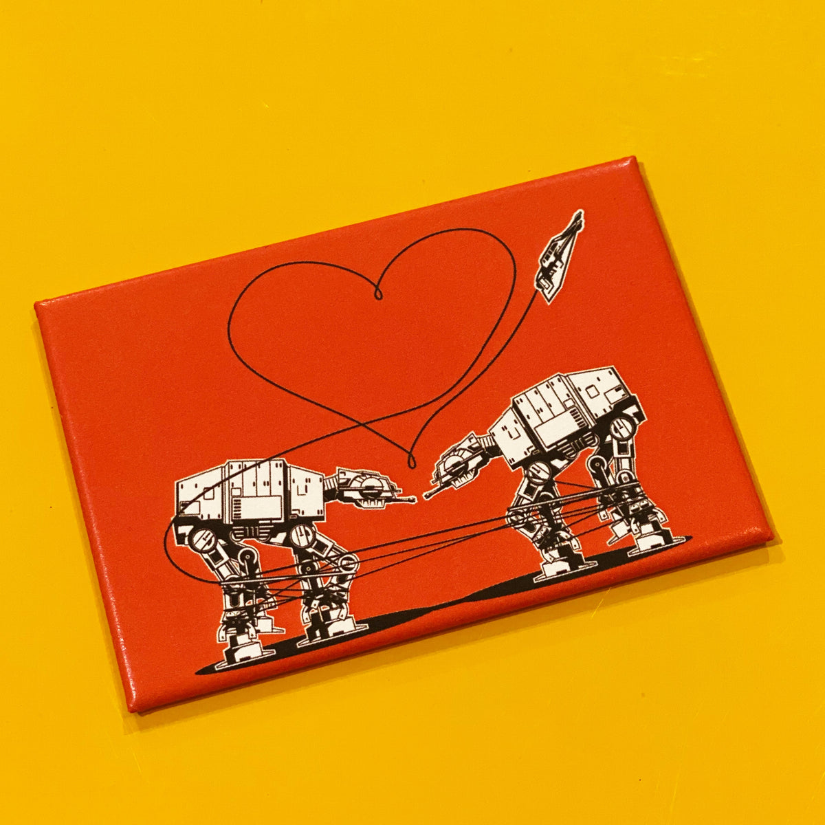 Orange rectangular magnet with an illustration of two AT-ATs from Star Wars with a heart above them, against a yellow backdrop. 