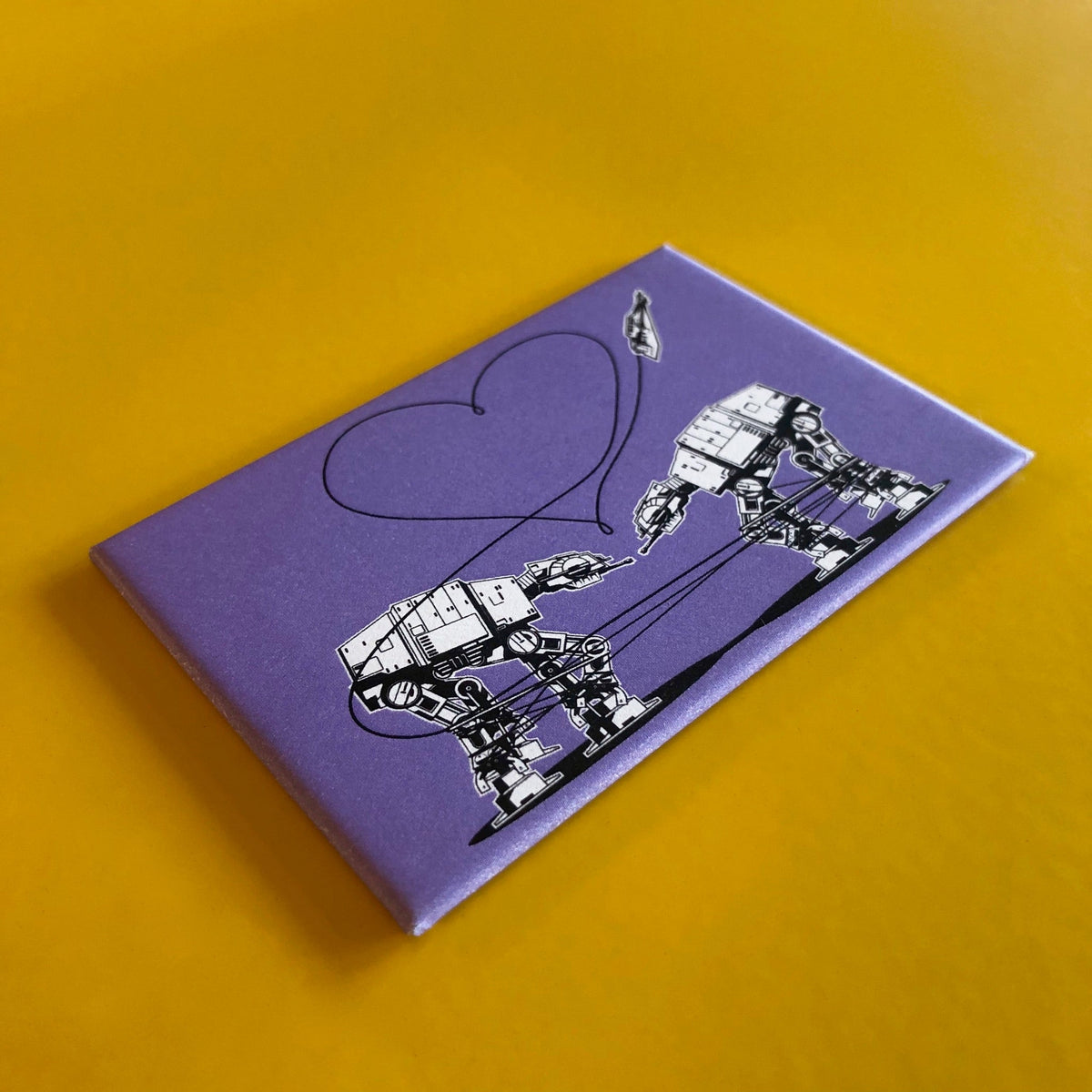 Purple rectangular magnet with an illustration of two AT-ATs from Star Wars with a heart above them against a yellow backdrop. 