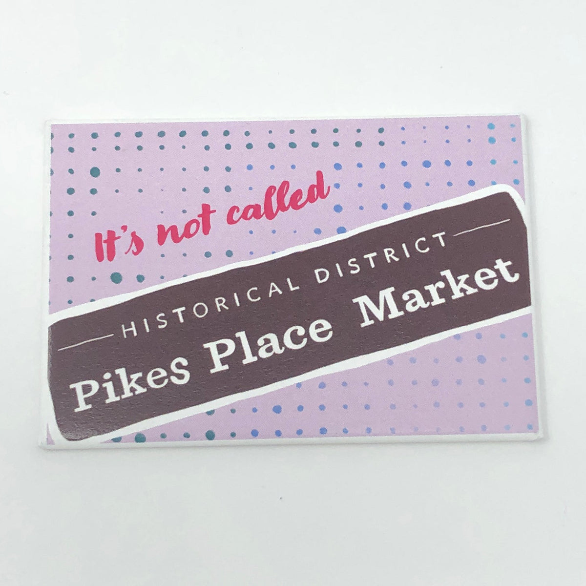 A pink rectangular magnet with text that says "it's not called (Historical District) Pikes Place Market"