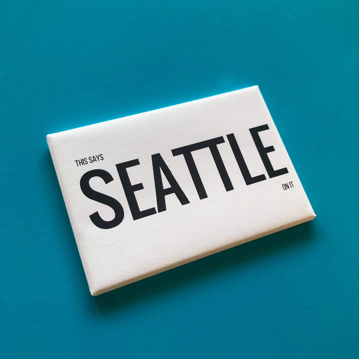 White rectangular magnet with text that says "THIS SAYS SEATTLE ON IT" against a blue background. 