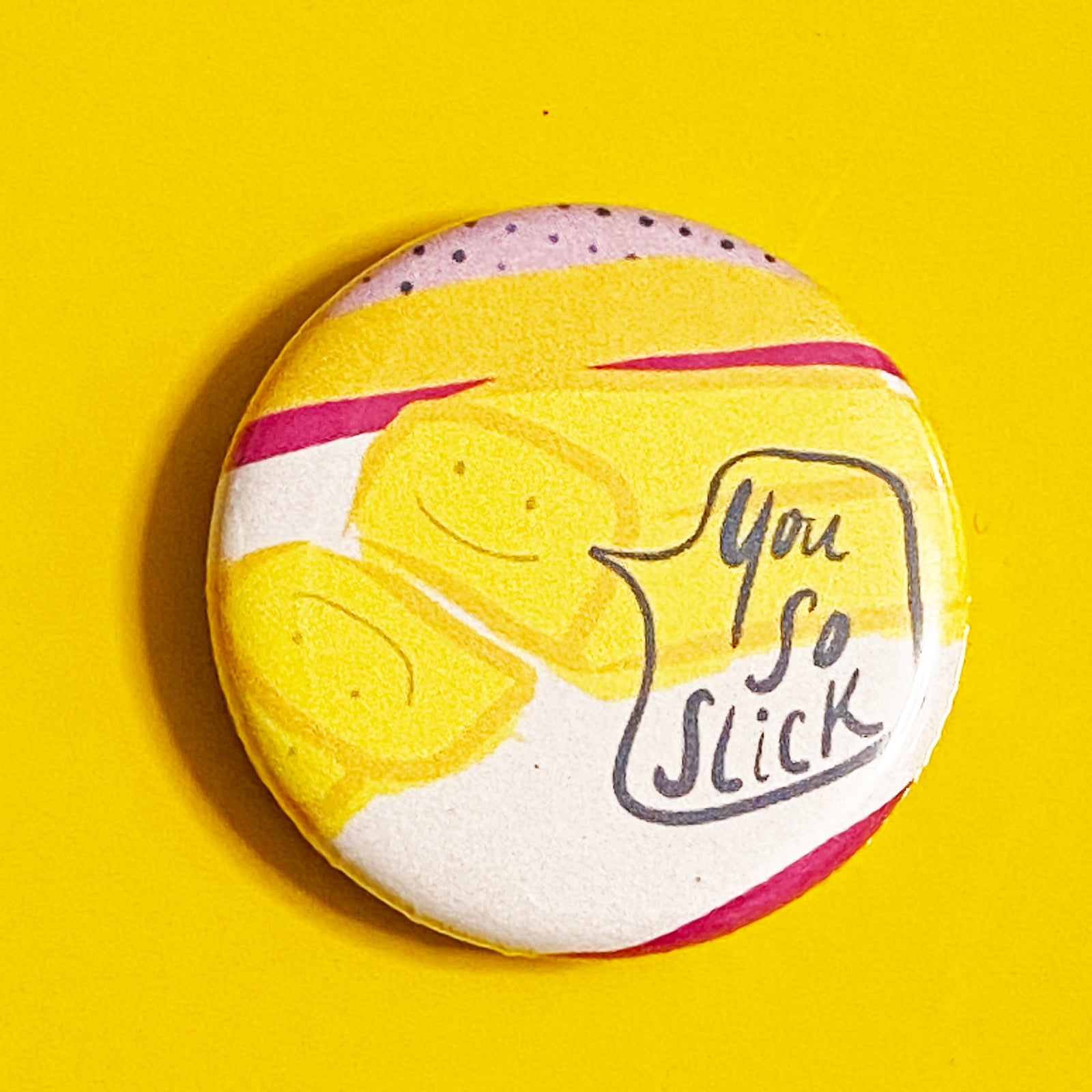A round magnet with an illustration of a stick of butter with a speech bubble that says "You so slick" against a yellow background. 