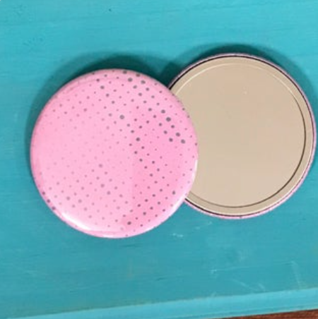 Two mirrors against a blue background- one face up showing its reflective side, and one face down, showing a pattern of dots on a pink background. 