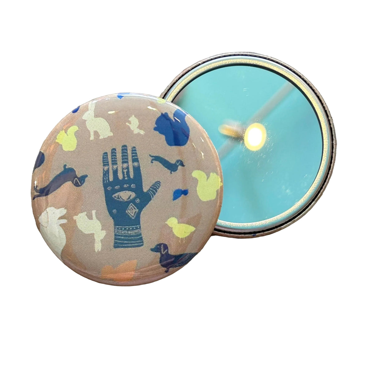 Two mirrors against a white background, one face up showing its reflective side, and the other face down showing a design of a hand with an eye on it surrounded by various illustrated animals. 