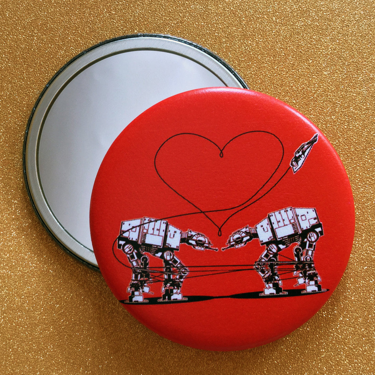 Red round mirror with a design of two AT-ATs from Star Wars with a heart above them, against a glittery gold backdrop
