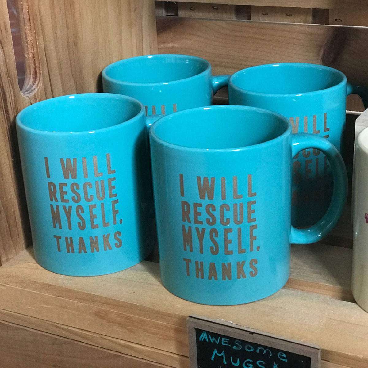 Group of four teal mugs sitting on a wooden shelf with gold text on them that reads "I WILL RESCUE MYSELF, THANKS"