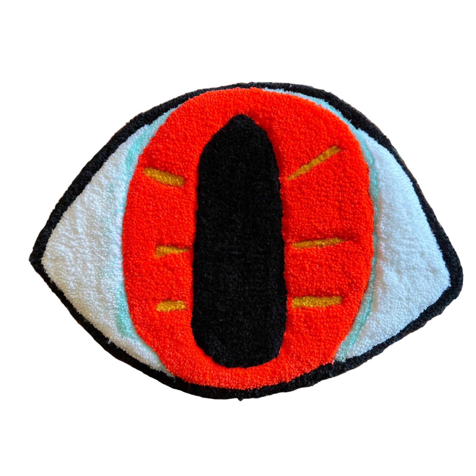 A tufted art piece in the shape of an eye with a black outline and pupil, and an orange iris with yellow stripes against a brick background. 