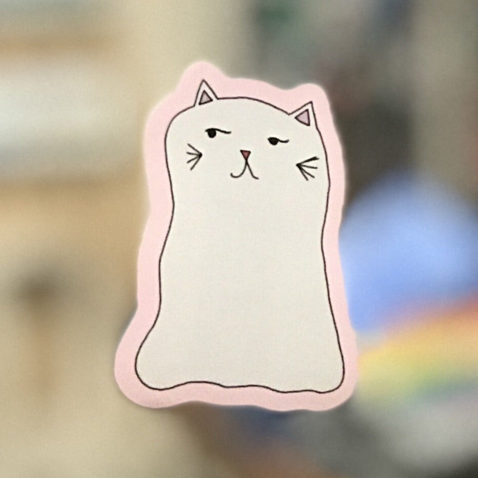 A sticker of a cat in the shape of a ghost against a blurred background. 