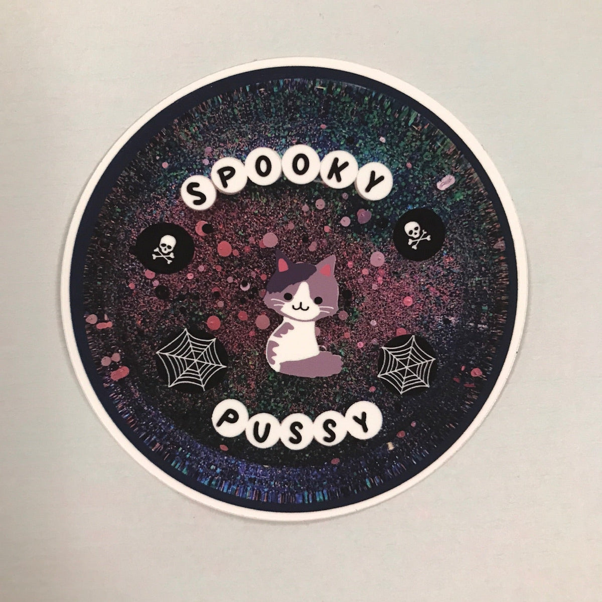 Circular sticker with 'Spooky Pussy' text and cat illustration on a gradient background