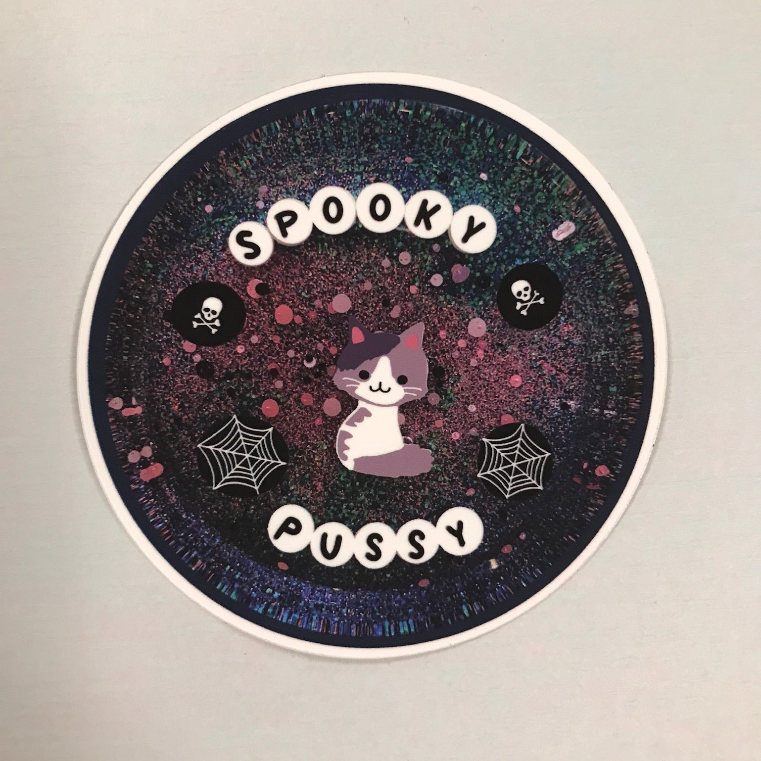 Circular sticker with 'Spooky Pussy' text and cat illustration on a gradient background