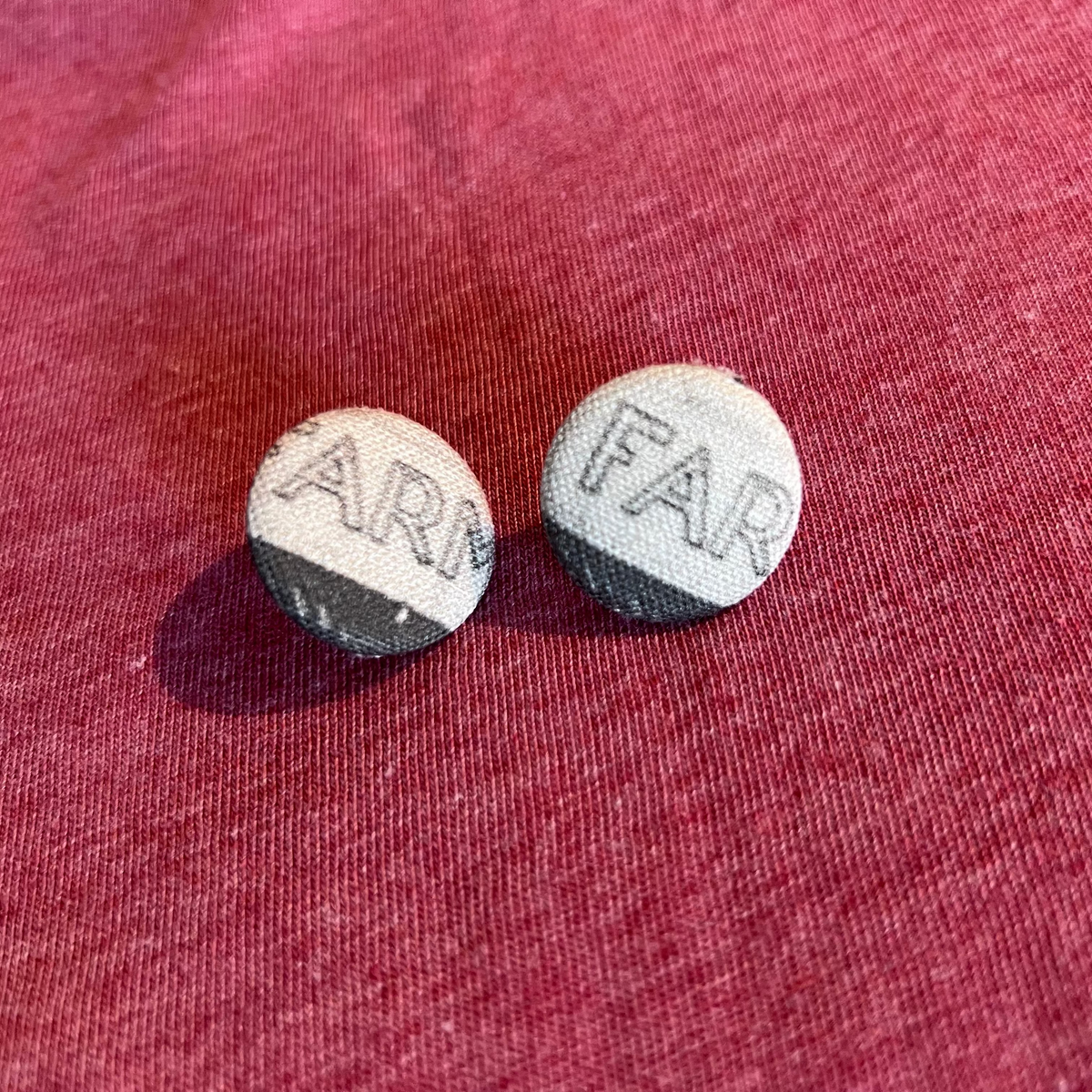 Two round earrings with black text on a red fabric background