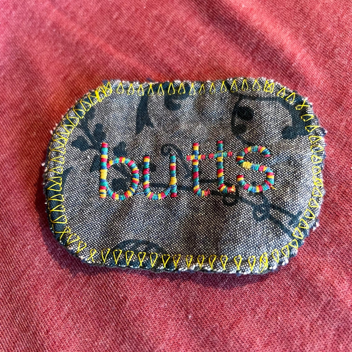 Embroidered patch that says "butts" in rainbow thread.